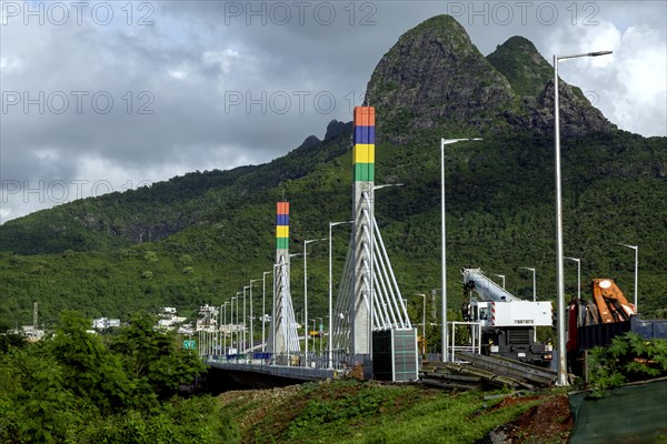 A highway with Mauritian emblem on pillar and a truck driving, surrounded by mountains and an