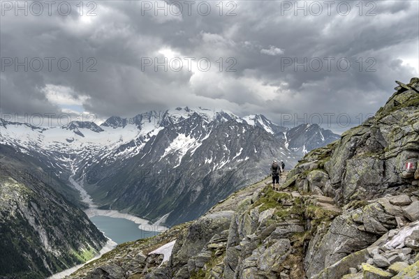 Two mountaineers on hiking trail with snow, view of Schlegeisspeicher, glaciated rocky mountain