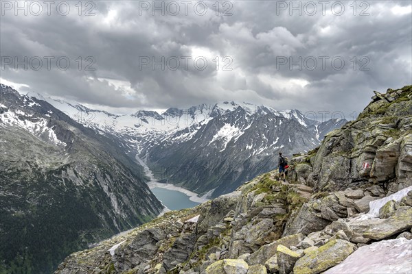 Mountaineer on hiking trail, view of Schlegeisspeicher, glaciated rocky mountain peaks Hoher
