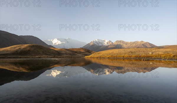 White glaciated and snowy mountain peak Pik Lenin at sunrise, mountains reflected in a lake between