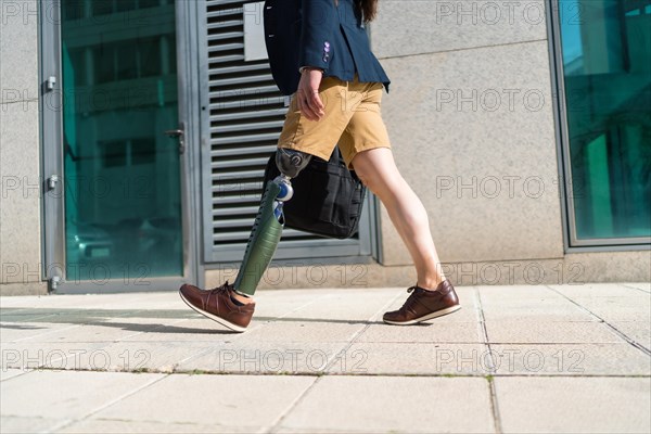 Lower part of an unrecognizable businessman with prosthetic leg walking along a financial district
