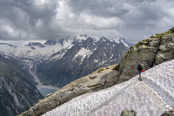 Mountaineer on hiking trail with snow, view of Schlegeisspeicher, glaciated rocky mountain peaks