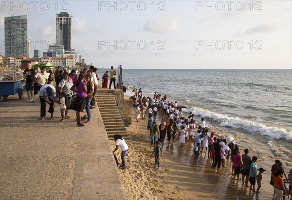 School children paddle in the sea on small sandy beach at Galle Face Green, Colombo, Sri Lanka,
