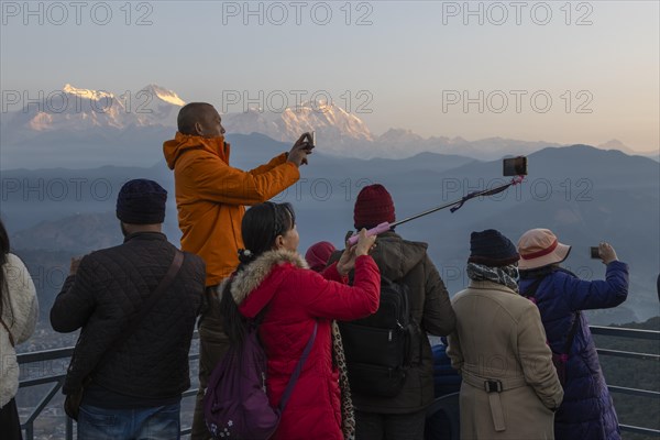 Asian-looking tourists watching and photographing sunrise as well as shooting selfies on the second
