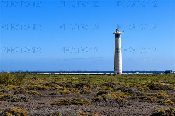 View of lighthouse Faro de Morro Jable on east coast of peninsula Jandia, in the foreground green