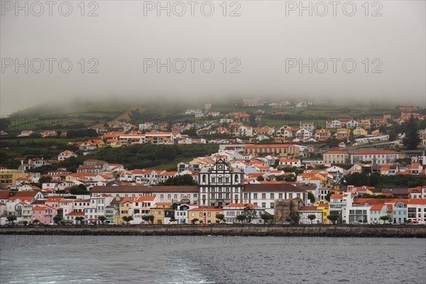 The coastal town of Horta under the fog, colourful houses nestle against green hills with calm sea