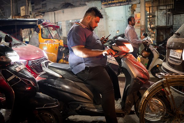 Man on scooter standing in a traffic jam looking at his mobile phone, Hyderabad, Andhra Pradesh,