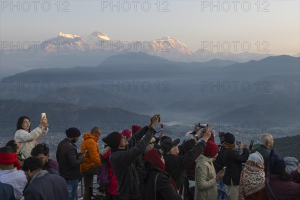 Asian-looking tourists watching and photographing sunrise as well as shooting selfies on the second