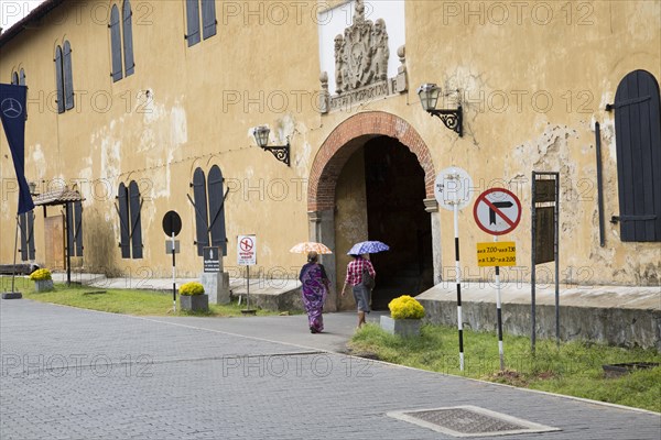 Women walking with umbrellas for shade towards the fort doorway exit in the historic town of Galle,