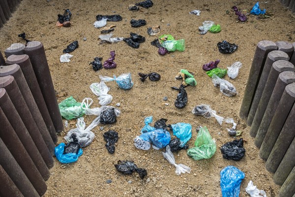 Fenced sandy public dog toilet area in city park filled with colourful discarded plastic dog poop