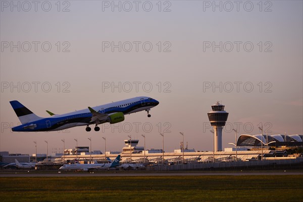 AirBaltic Airbus A220 taking off on Runway South with Terminal 1 and Tower in the sunset, Munich