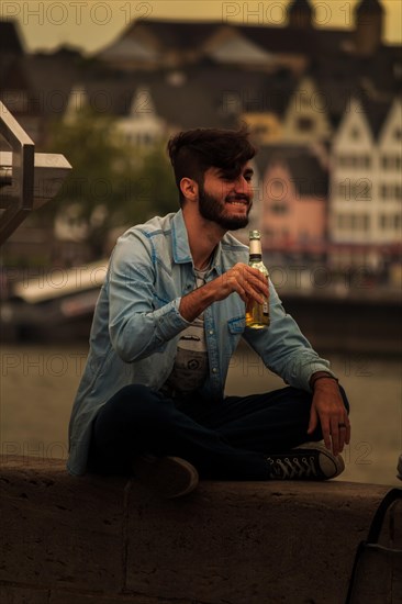 A man sits on the riverbank enjoying a drink in the evening, Hohenzollernbruecke, Cologne Deutz,