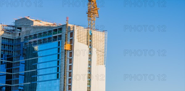 Yellow crane elevator attached to side of building that is under construction against a clear blue