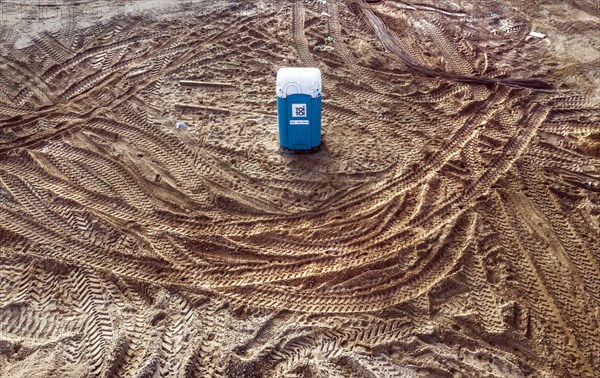 Traces of truck tyres and construction machinery circle a toilet in the middle of a construction