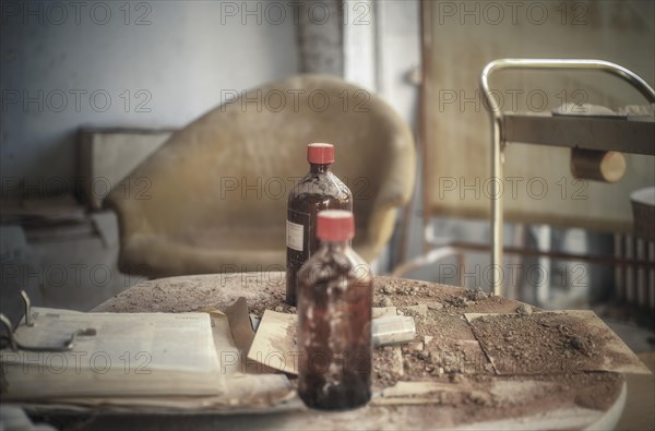 An old cloudy bottle on a dirty table next to a rusty hospital trolley, urologist's villa Dr Anna L