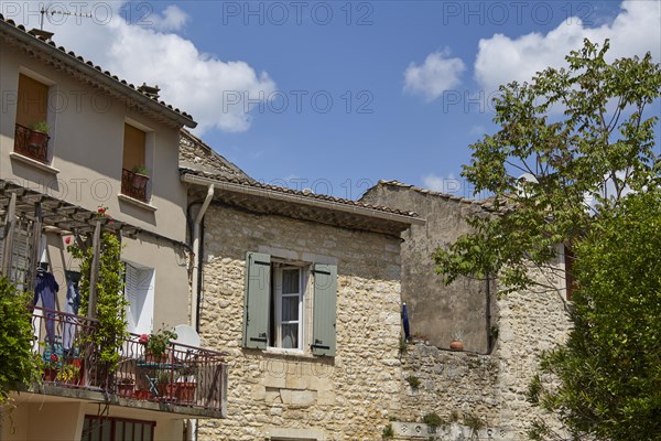 Old sandstone-walled houses with windows, shutters, balcony and a balcony in Goudargues, Gard
