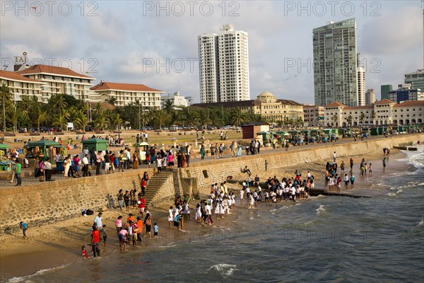 School children paddle in the sea on small sandy beach at Galle Face Green, Colombo, Sri Lanka,