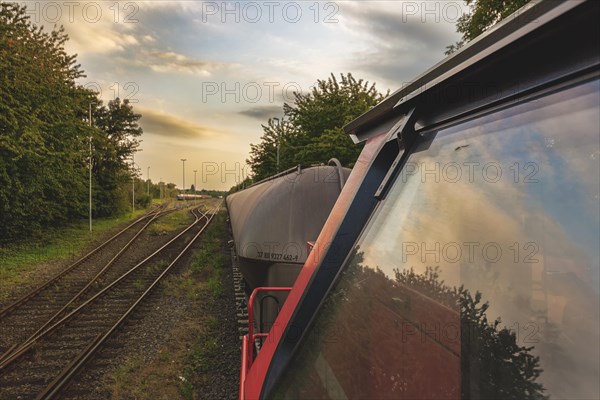 View from the rear-view mirror of a locomotive onto a goods train and tracks in the evening light,