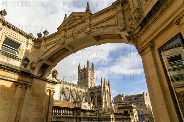 View of abbey church and Roman Baths from under stone archway, York Street, Bath, Somerset,