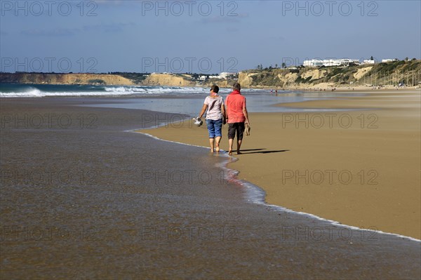 Man and woman walking together on sandy beach at Conil de la Frontera, Cadiz Province, Spain,