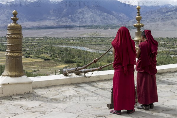 Monks playing Tibetan horns, dungchens, standing on the roof of Thikse Gompa, a large, Buddhist