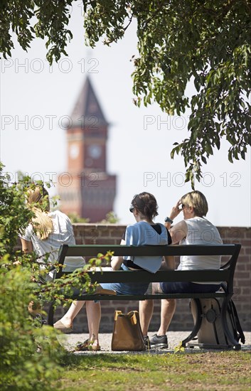 Swedish woman sitting on a park bench, behind them the tower of the town hall, Helsingborg, Skane
