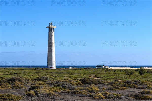 View of lighthouse Faro de Morro Jable on east coast of peninsula Jandia, in the foreground green