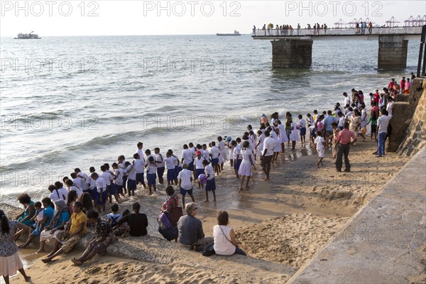 School children paddle in the sea on small sandy beach at Galle Face Green, Colombo, Sri Lanka,