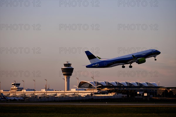 AirBaltic Airbus A220 taking off on Runway South with Terminal 1 and Tower in the sunset, Munich