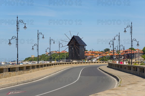 A tidy coastal road leads to a traditional windmill under a bright blue sky, Historic windmill on