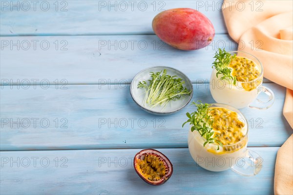 Mango yogurt with passionfruit and cilantro microgreen in glass on blue wooden background with