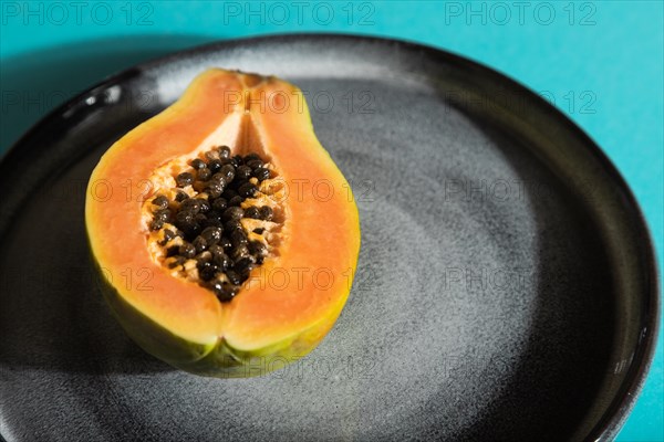 Ripe cut papaya on gray plate on blue pastel background. Side view, close up, hard light. Tropical,