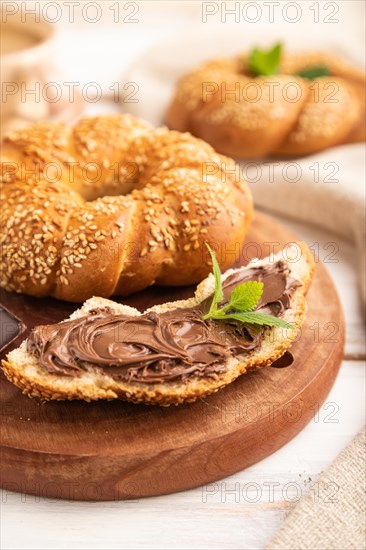 Homemade sweet bun with chocolate cream and cup of coffee on a white wooden background and linen