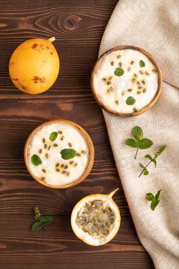 Yoghurt with granadilla and mint in wooden bowl on brown wooden background and linen textile. top