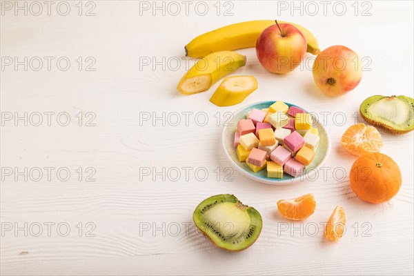 Various fruit jelly chewing candies on plate on white wooden background. apple, banana, tangerine,