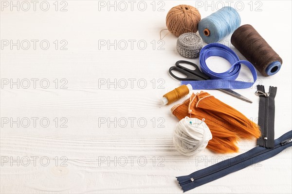 Sewing accessories: scissors, thread, thimbles, braid on white wooden background. Side view, copy