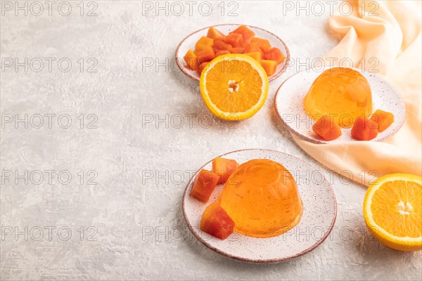 Papaya and orange jelly on gray concrete background and orange linen textile. side view, flat lay,