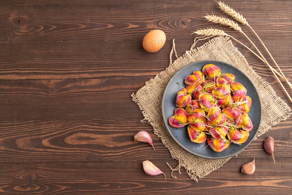 Rainbow colored dumplings with pepper, herbs, microgreen on brown wooden background and linen