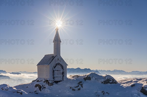 Small chapel with sun star on snowy mountain peak, backlight, winter, chapel on Hochgern, Chiemgau