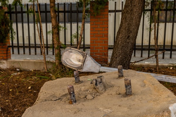 Old dismantled streetlight removed from lamppost and laying on ground behind concrete streetlamp