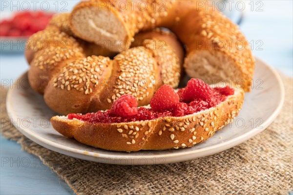 Homemade sweet bun with raspberry jam and cup of coffee on a blue wooden background and linen