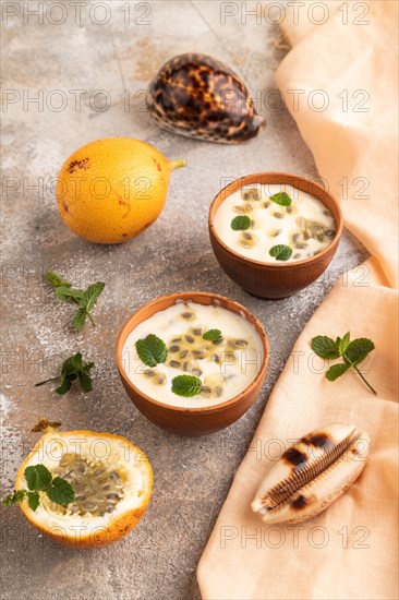 Yoghurt with granadilla and mint in clay bowl on brown concrete background and orange linen textile