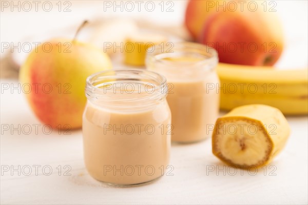 Baby puree with fruits mix, apple, banana infant formula in glass jar on white wooden background.
