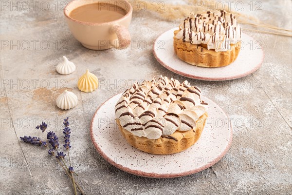 Two tartlets with meringue cream and cup of coffee on brown concrete background. side view.