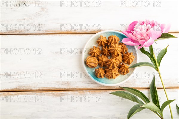 Homemade soft caramel fudge candies on blue plate on white wooden background, peony flower