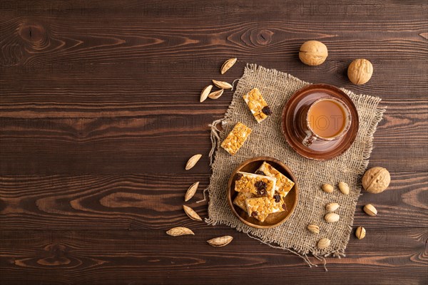 Traditional candy nougat with nuts and sesame with cup of green tea on brown wooden background and