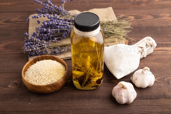 Sunflower oil in a glass jar with various herbs and spices, lavender, sesame, rosemary on a brown