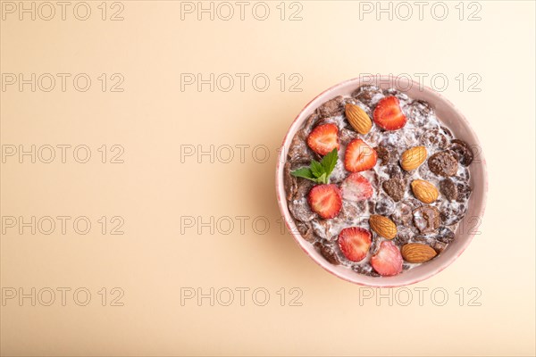 Chocolate cornflakes with milk, strawberry and almonds in ceramic bowl on pastel orange background.