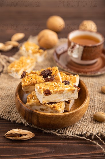 Traditional candy nougat with nuts and sesame with cup of green tea on brown wooden background and