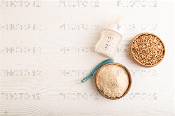 Powdered milk and buckwheat baby food mix, infant formula, pacifier, bottle, spoon on white wooden